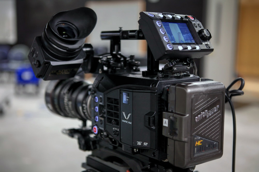 Professional cinema camera with a large lens, external monitor, and battery pack on a rig.